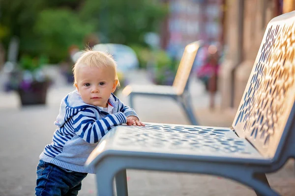 Carino bambino, in piedi accanto a una panchina nella bella città — Foto Stock