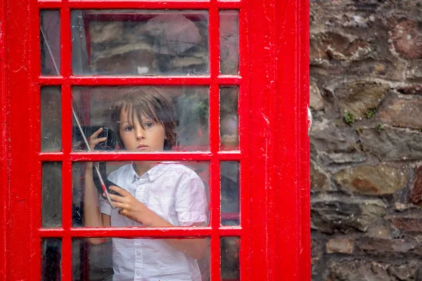Lindo chico, niño, llamando desde una cabina telefónica roja en la ciudad — Foto de Stock