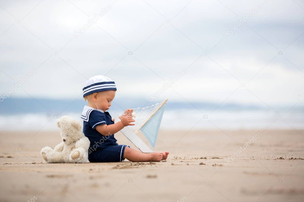 Baby boy sitting on the beach near the water and plays with a to