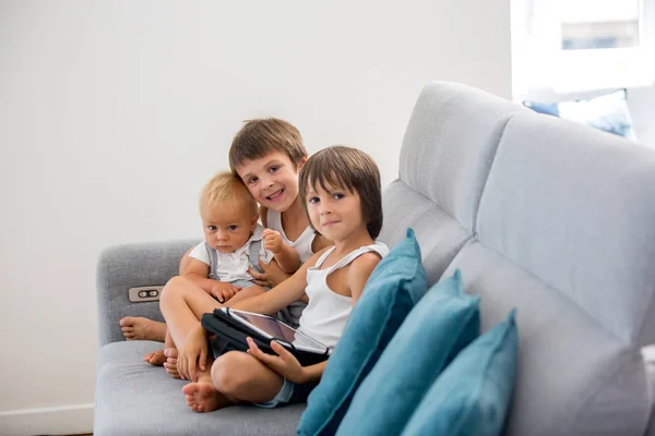 Sweet children, sitting on couch in sunny living room, playing o — Stock Photo, Image