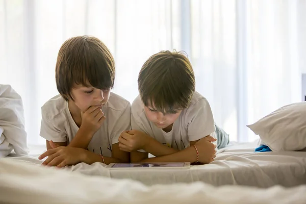 Brüder spielen im Bett auf dem Tablet, genießen den Sommerurlaub — Stockfoto