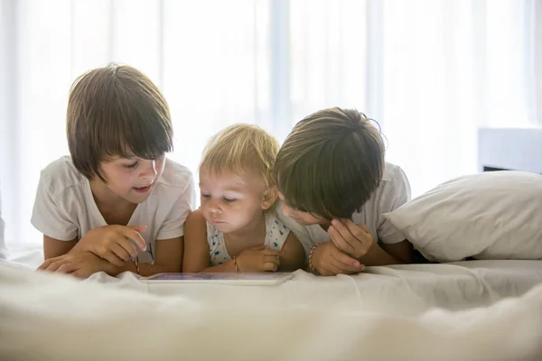 Hermanos, jugando en la cama en la tableta, disfrutando de vacaciones de verano —  Fotos de Stock