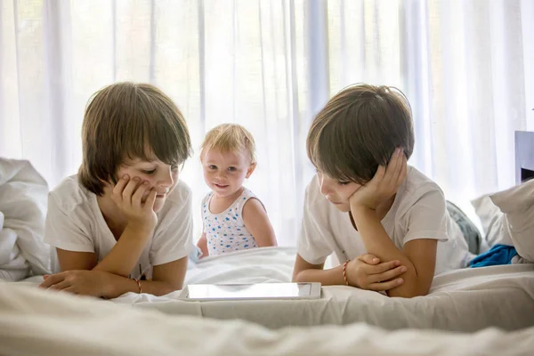 Hermanos, jugando en la cama en la tableta, disfrutando de vacaciones de verano — Foto de Stock