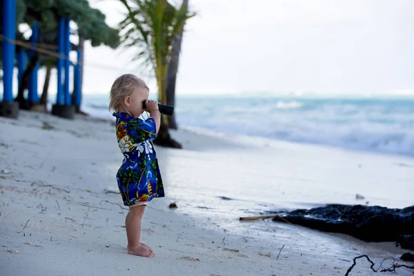 Doce menino olha através de binóculos, observando a vida no oceano um — Fotografia de Stock