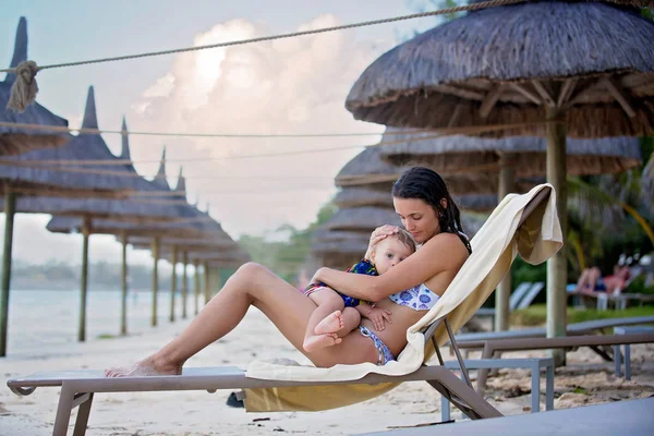 माँ, समुद्र तट पर अपने छोटे बच्चे को स्तनपान कर रही है, टी पर गले लगा रही है — स्टॉक फ़ोटो, इमेज