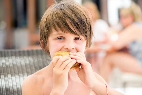 Doux garçon d'âge préscolaire, manger hamburger frais dans un restaurant sur b — Photo