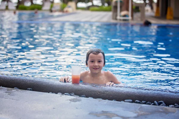 Χαριτωμένο αγόρι, πίνοντας κοουρίτσα στην πισίνα, ενώ σε διακοπές σε τροπικό — Φωτογραφία Αρχείου