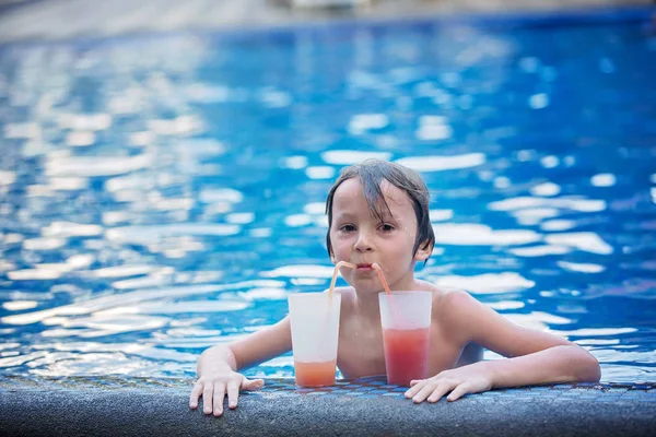 Симпатичный мальчик, пьет коктейль в бассейне во время отдыха в тропиках — стоковое фото