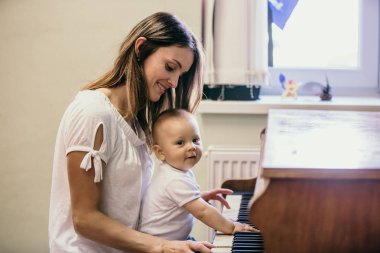 Anne ve yeni yürümeye başlayan erkek bebek, evde piyano çalıyor