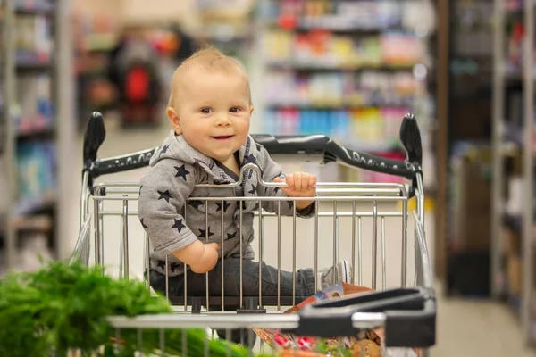 Menino bebê, sentado em um carrinho de compras na mercearia, s — Fotografia de Stock