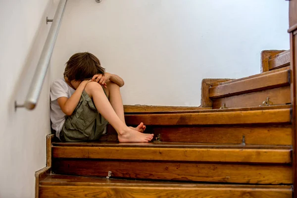 Niño triste, sentado en una escalera en una casa grande, concepto para bu —  Fotos de Stock