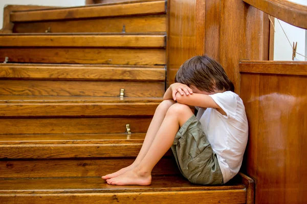 Niño triste, sentado en una escalera en una casa grande, concepto para bu —  Fotos de Stock