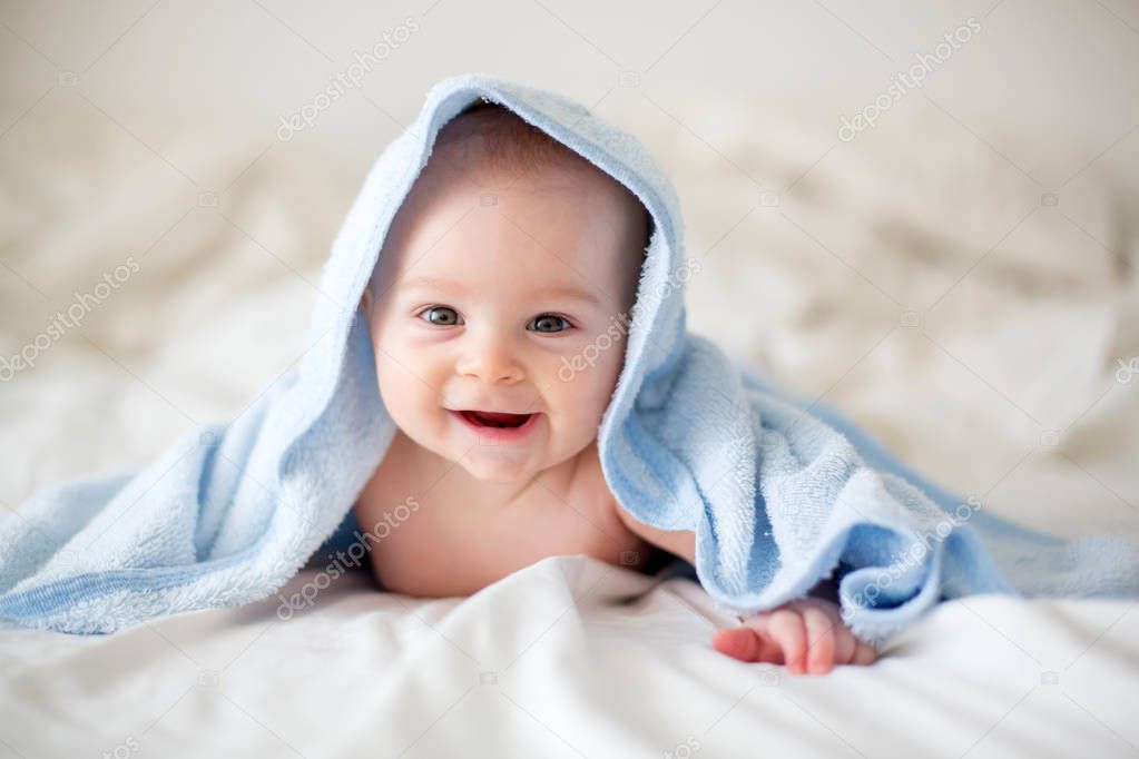 Cute little baby boy, relaxing in bed after bath, smiling happil