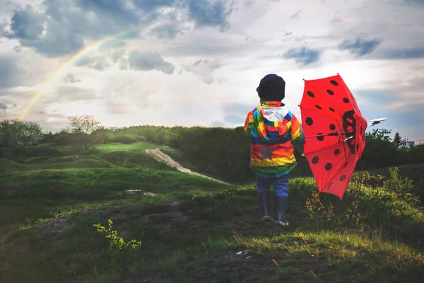 Beau petit garçon avec imperméable arc-en-ciel, profitant de la pluie , — Photo