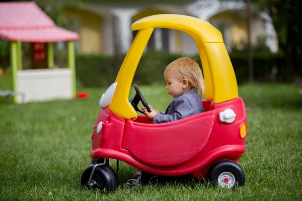 Carino bambino ragazzo, equitazione grande plastica rosso auto giocattolo nel parco — Foto Stock