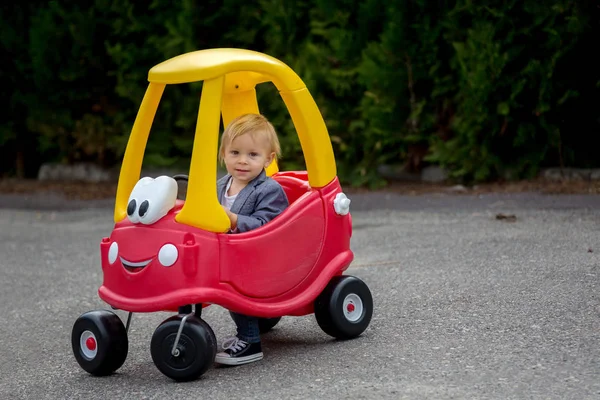 Lindo niño pequeño, montar gran juguete de plástico coche rojo en el parque — Foto de Stock