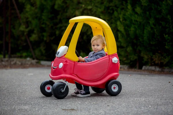 Lindo niño pequeño, montar gran juguete de plástico coche rojo en el parque — Foto de Stock