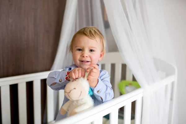 Portræt af keder baby stående i krybbe. Baby dreng stå alene i - Stock-foto