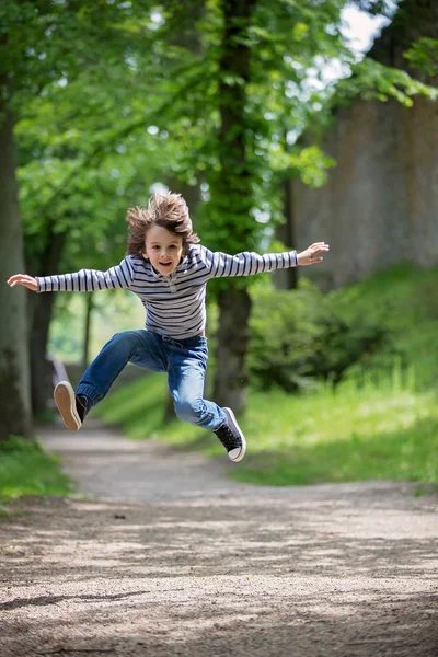 Niño feliz, chico, corriendo y saltando en el camino en el parque con el árbol —  Fotos de Stock