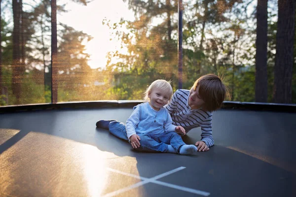 Słodki preteen chłopiec i jego brat maluch skakanie na trampoliny. — Zdjęcie stockowe