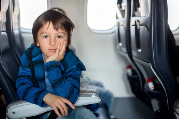 Söt förskolebarn, tittar genom fönstret i flygplan, medan — Stockfoto