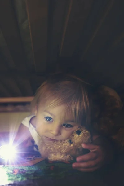 Маленька дитина, ховається під ліжком, обіймаючи плюшевого ведмедя і голоді — стокове фото