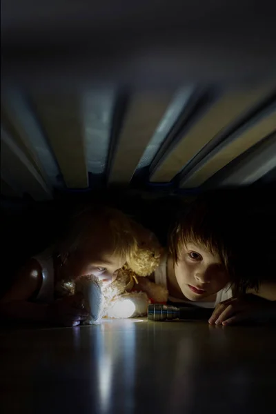 Klein kind, verstopt onder het bed, knuffelen teddybeer en holdi — Stockfoto