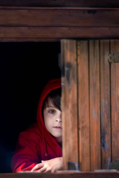 Preteen garçon en sweat-shirt rouge, caché derrière une porte en bois, regardez — Photo