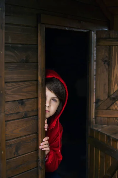 Preteen jongen in rode Sweatshirt, verbergen achter een houten deur, kijk — Stockfoto