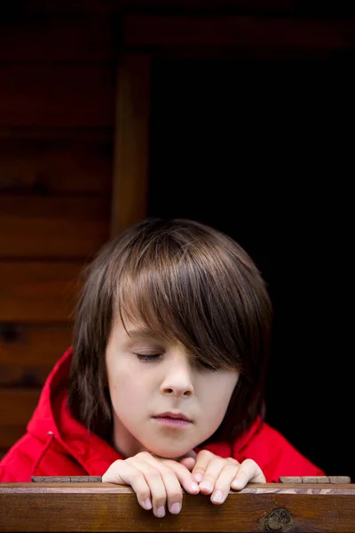 Preteen boy in red sweatshirt, hiding behind a wooden door, look — Stock Photo, Image