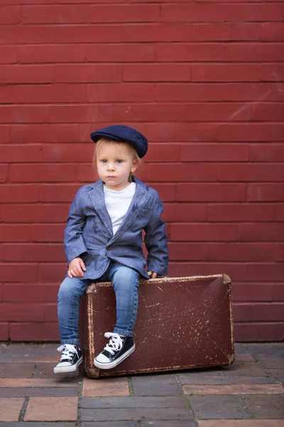 Cute little toddler child, sitting on a vintage suitcase in fron — Stock Photo, Image