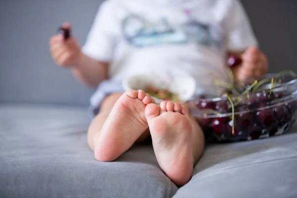 Dolce bambino ragazzo, seduto su un divano, mangiare ciliegie — Foto Stock