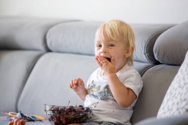 Tatlı Toddler çocuk, bir kanepede oturan, kiraz ve Looki yeme