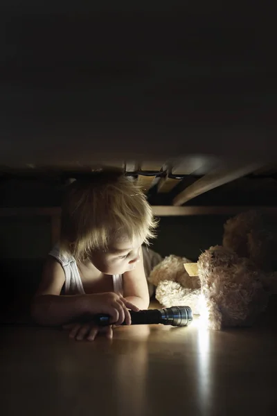 Küçük çocuk, yatağın altında saklanıyor, oyuncak ayıya ve holdi'ye sarılıyor. — Stok fotoğraf