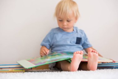 Tatlı yürümeye başlayan çocuk, evde kitap okuyor, yerde oturuyor, 