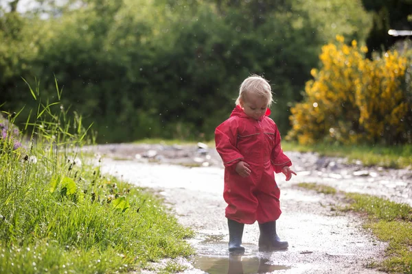 Lieve kleine peuter jongen, blond kind in rode regenjas en blauw b — Stockfoto