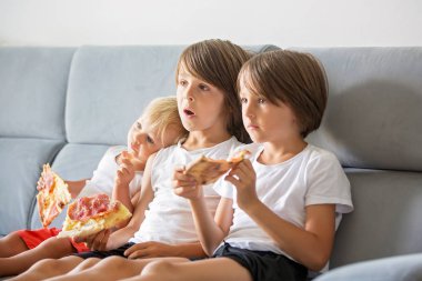 Sevimli çocuklar, kanepede oturan, pizza yemek ve Tv izlerken.