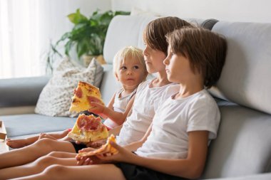 Sevimli çocuklar, kanepede oturan, pizza yemek ve Tv izlerken.