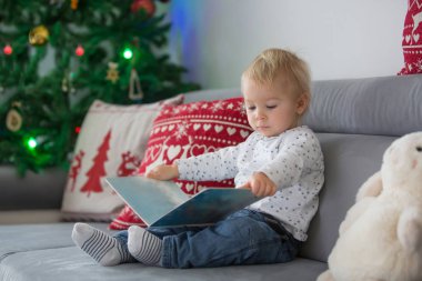 Sevimli yürümeye başlayan çocuk, kanepede oturan, Ch önünde bir kitap okuma