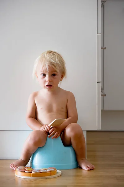 Малыш, сидящий на горшке, играющий с деревянной игрушкой — стоковое фото