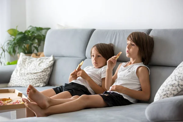 Crianças bonitas, sentadas no sofá, comendo pizza e assistindo TV. H — Fotografia de Stock