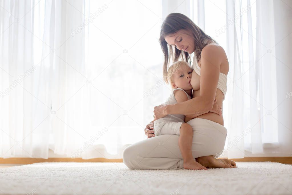 Young mother breastfeeding her toddler baby boy at home 