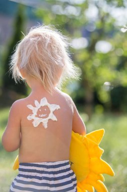 Sırtında güneş şeklinde güneş losyonu olan yeni yürümeye başlayan çocuk, goin