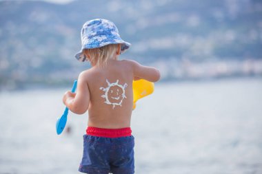 Tatlı okul öncesi çocuk, sunscream uygulanan tüplü maske tutarak o