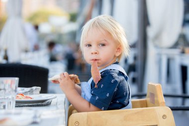 Sevimli yürümeye başlayan çocuk, bir restoranda yüksek sandalyede oturan, yemek 