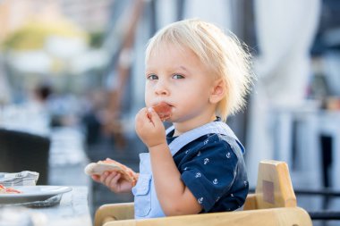 Sevimli yürümeye başlayan çocuk, bir restoranda yüksek sandalyede oturan, yemek 