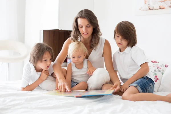 Jovem mãe, leia um livro para seus três filhos, meninos, no ser — Fotografia de Stock