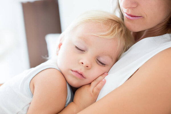 Young mother lying in bed with her sleeping toddler baby boy 