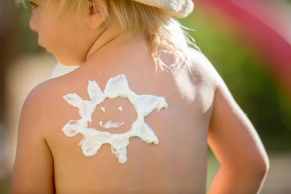 Toddler child with suntan lotion shaped as sun on his back, goin