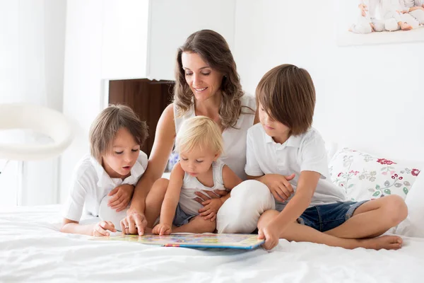 Junge Mutter, las ihren drei Kindern, Jungen, ein Buch in der Bibliothek — Stockfoto